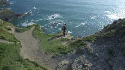 Aerial view of man with backpack on top of a cliff in front of the ocean - Old Head of Kinsale, Ireland