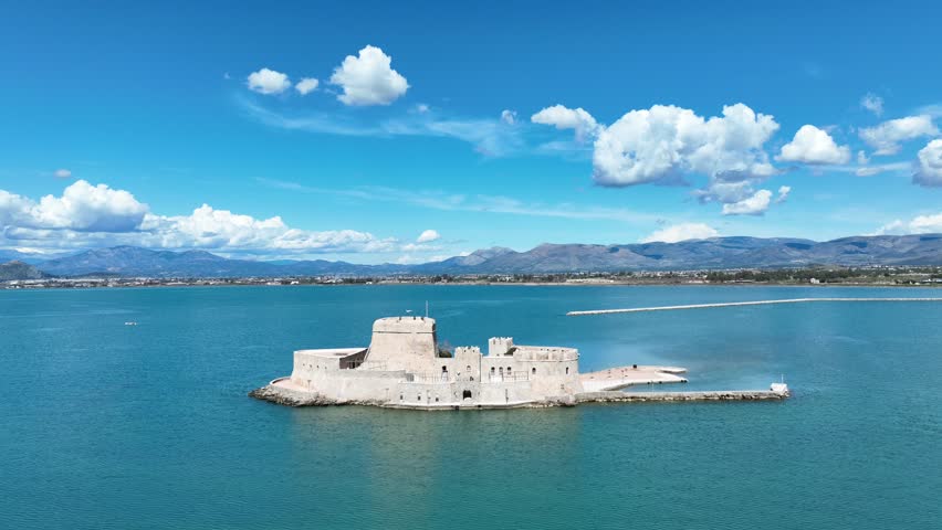 Aerial drone cinematic video of castle of Bourtzi built at sea a popular attraction in city of Nafplio as seen in the morning with nice white clouds and deep blue sky, Argolida, Greece