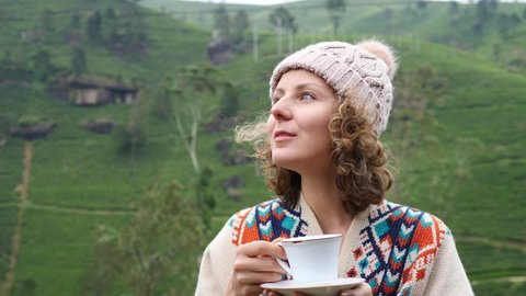 Young Woman In Knit Hat Smelling Tea In Cup Outdoors At Tea Plantation Hills. Closeup Portrait. 4K.
