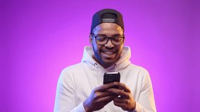 A delighted young man with a content smile sends texts from his smartphone, caught in a moment of joyful digital interaction against a vibrant purple background. Camera 8K RAW.  - Powered by Shutterstock - Get 15% off with code: PIKWIZARD15