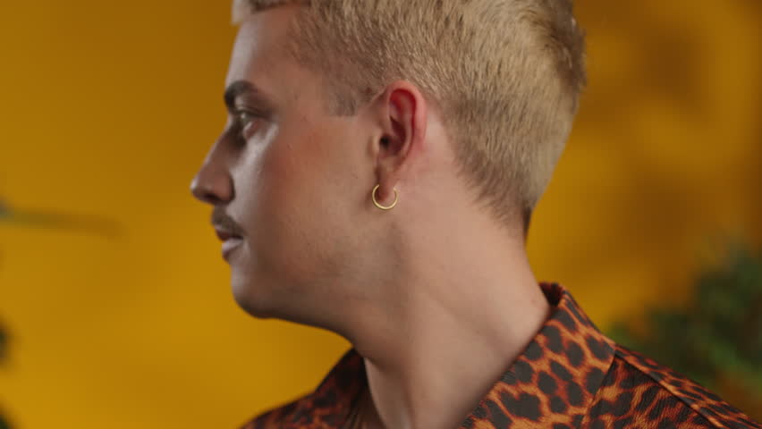 Close-up portrait of young gay man with makeup in leopard shirt looking at camera