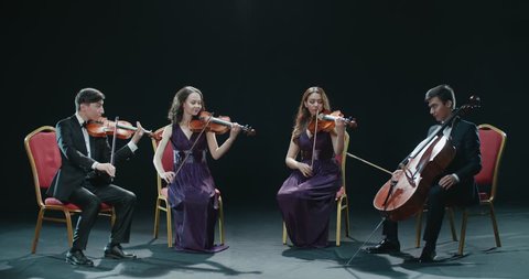 classical string quartet during the performance of the symphony, abstract black background in the studio
