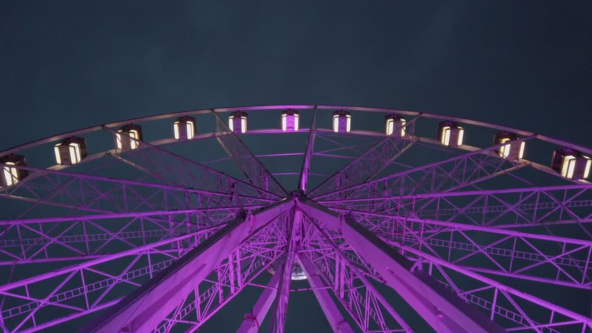 Purple ferris wheel wide shot, ground level up shot in night time. Lyon ferris wheel, place Bellecour, France. Cloudy night sky.