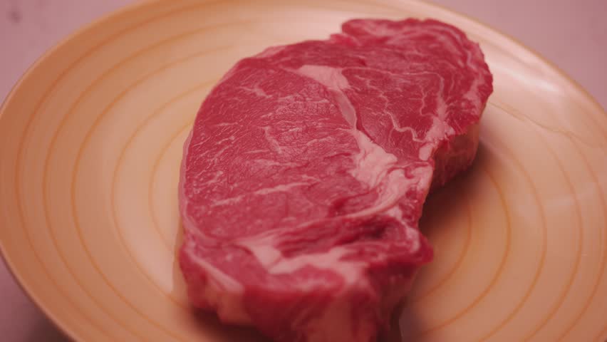 Fresh raw beef bone rib roughly close up. Fresh piece of raw red meat. Close-up macro shot of a fillet texture. Slider along uncooked beefsteak. Ribeye meat or marbled beef. Steak for restaurants.