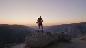 Amazing view of dark mountain range with orange skyline, happy male hiker on a stone on a summit raising hands up with delight, overwhelmed with emotions. High quality 4k footage