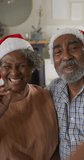 Vertical shot of a senior African American couple having a video call, wearing Santa Clause hats. Seniors, technology, and Christmas concept.