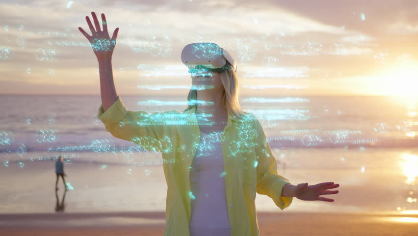 Attractive young female using futuristic augmented reality software interface standing outdoors at ocean beach. Woman wearing headset to look at VFX Animation with futuristic project at scenic sunset