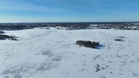 Drone video over a frozen lake during daytime with small islands and trees