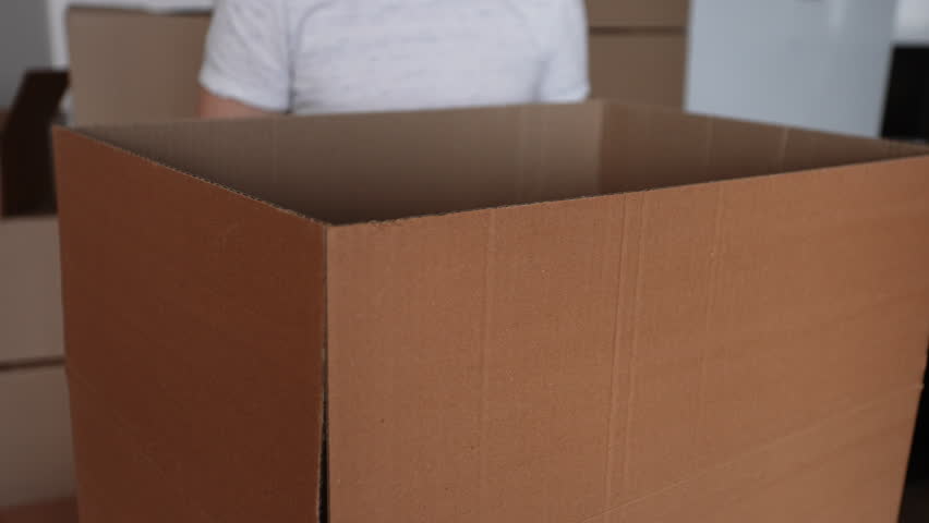 Close-up cropped shot of unrecognizable man packing big cardboard box for personal stuff storing at relocation day, leaves to new own or rented house, prepare dwelling for remodeling or removal work.
