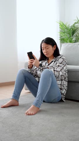Sad asian woman using phone in the living room. Frustrated young person looking at social media. Royalty-Free Stock Footage #3471927197