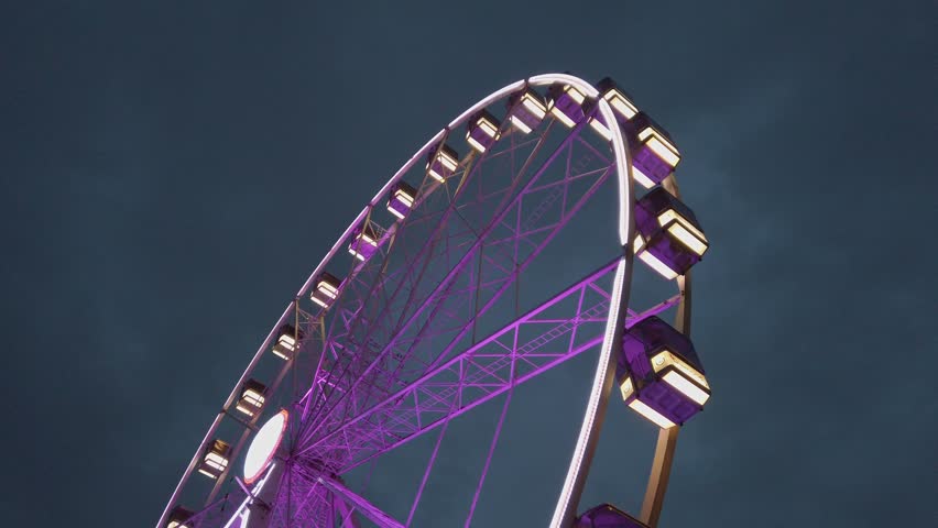 Purple ferris wheel medium shot, ground level side shot in night time. Lyon ferris wheel, place Bellecour, France. Cloudy night sky.