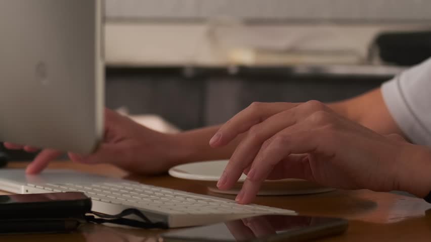 Beautiful fingers of female hands work at keyboard of personal computer at an office table next to a lying telephone, close-up. Office work