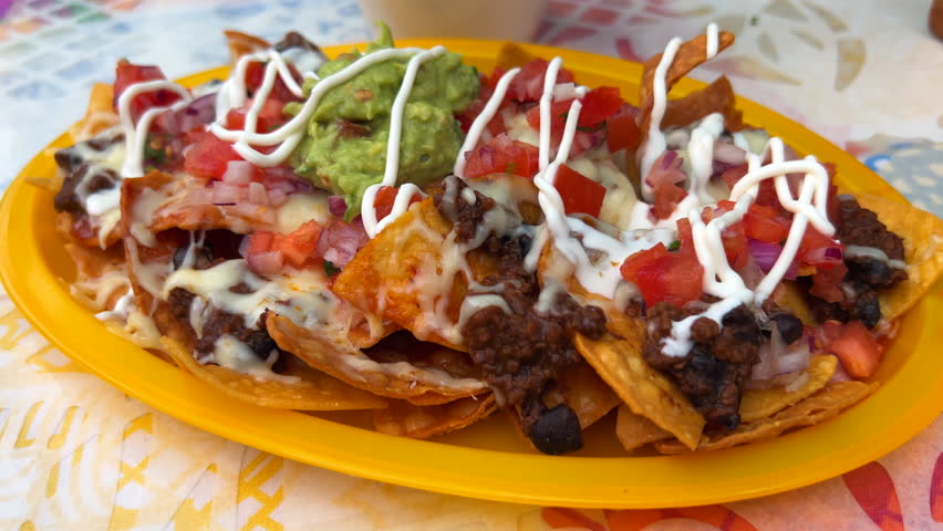 Eating traditional Tex-Mex Mexican nachos with beef chilli con carne, guacamole, melted cheese and sour cream, totopos tortilla chips, tasty food, 4K shot