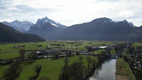 Drone clip showing Alpine mountain range with snow topped mountains and flat lowland below, on bright sunny Spring day