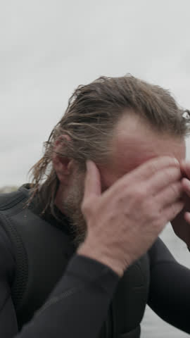 Vertical portrait of adult Caucasian male surfer with slicked back wet hair and beard looking at camera in water