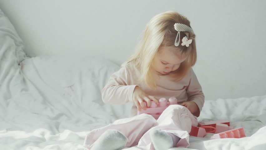 little girl sitting on bed and playing with constructor toy.