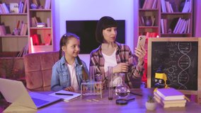 Caucasian mother educating little child daughter at home, during online video lesson. Small kid girl playing with young mom, involved in doing chemistry experiments together recording content for blog