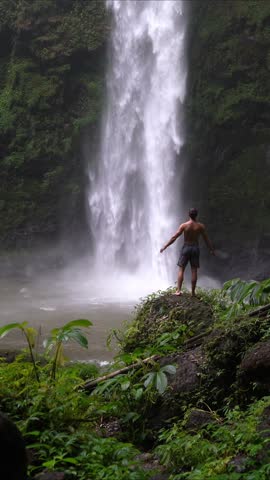 Man standing in front of waterfall. Amazing waterfall. Bali, Indonesia. Travel concept. Hidden paradise oasis. This waterfall is hidden in greenery environment. Water is falling down from above