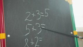 Teacher shows maths tasks written on chalkboard with pointer in classroom closeup. Simple mathematical problems for primary school students on blackboard - Powered by Shutterstock - Get 15% off with code: PIKWIZARD15