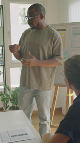 Vertical shot of black man standing by whiteboard and speaking to group of students while giving lesson