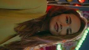 Smiling girl posing luna park carousel vertical video closeup. Dreamy model enjoying summer night at neon blinking lights. Romantic beautiful female looking camera waiting friends on street carnival - Powered by Shutterstock - Get 15% off with code: PIKWIZARD15