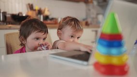 twin baby children playing laptop watching video in the kitchen lifestyle. happy family kid dream concept. baby twins playing video game on laptop looking at screen in kitchen