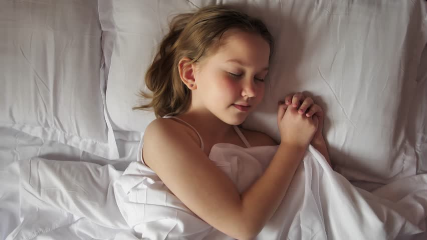Top view: Cute lovely 8 year old girl sleeping in a bed with white linen. The Caucasian girl calmly and carefree fell asleep in bed and had beautiful dreams. Comfortable sleep for a child.