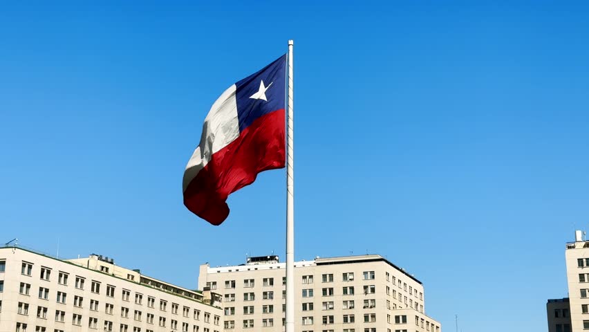 Chilean flag waving proudly against a clear blue sky, over cityscape backdrop