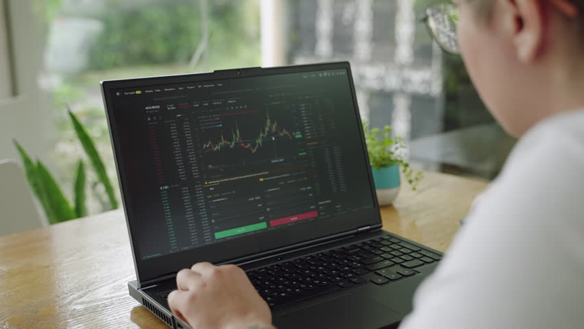 Professional day trader analyzes realtime chart data on laptop in modern office. Alert investor scrutinizes market trends for effective portfolio management. Analytical focus in trading environment.