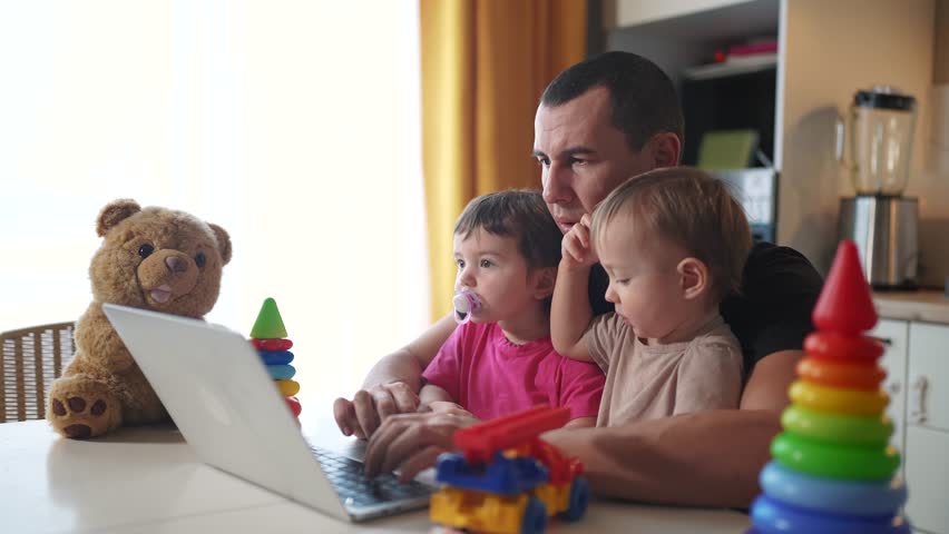 father working from home remotely with two baby in his fun arms. pandemic remote work business concept. father tries to work at home in kitchen, baby children interfere sitting on their hands Royalty-Free Stock Footage #3472510603