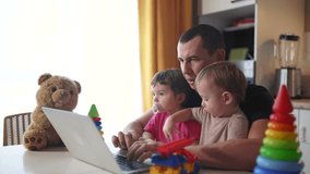 father working from home remotely with two baby in his fun arms. pandemic remote work business concept. father tries to work at home in kitchen, baby children interfere sitting on their hands - Powered by Shutterstock - Get 15% off with code: PIKWIZARD15