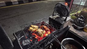 4k video footage of Indonesian street food seller is making traditional grilled chicken meat using burning charcoal and electric fan. Cooking process of roasted chicken.