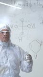 An elderly Caucasian male chemist in a protective suit writes on glass. Vertical video. 