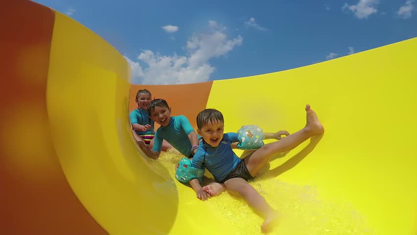 Laughing children ride together water slide on sunny day. High quality 4k footage