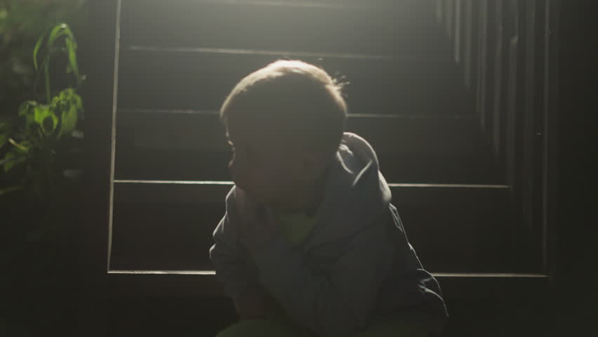 Preschooler child silhouette on stairs in evening. Cute boy sits alone on steps at cottage house. Kid rests on staircase of eco hotel at backlight