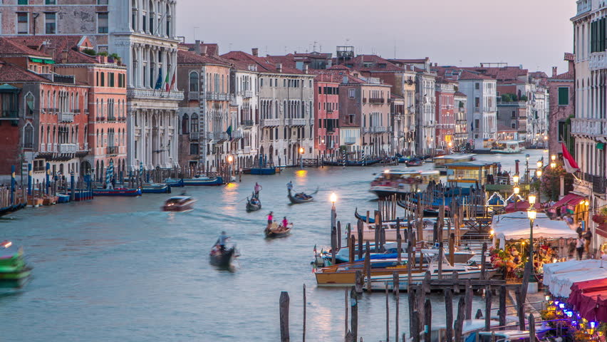 Grand Canal in Venice, Italy day to night transition timelapse. View from above on gondolas and city lights from Rialto Bridge. Beautiful and romantic Italian city on water.