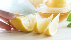 Closeup 4k footage of female hand cutting fresh lemons for lemonade on white wooden desk