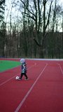 Small baby boy plays with a ball on the stadium. Child runs by the track kicking the ball. Vertical video.
