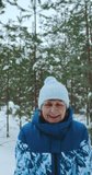 vertical video, a happy adult woman of 60-70 years old rejoices at her retirement, walks in a fresh snowy forest, throws snowflakes with her hands up and rejoices at the falling snow. High quality 4k