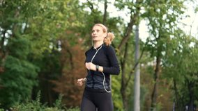 Happy female runner jogging in urban city park and looking smart watch. Sportswoman using fitness tracker. Woman checking result. Fit lady in headphones and tracksuit enjoys running outdoors in nature - Powered by Shutterstock - Get 15% off with code: PIKWIZARD15