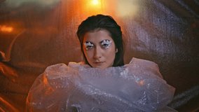 Wrapped in bubble wrap woman showcasing innovative eyelash art closeup. Mysterious gaze with floral makeup intensifying surreal fantasy ambiance. Portrait of individuality and contemporary fashion. - Powered by Shutterstock - Get 15% off with code: PIKWIZARD15