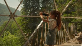 Child record video of nature at glamping. Little girl with camera shoots forest scene at eco hotel. Kid plays videographer on summer vacation