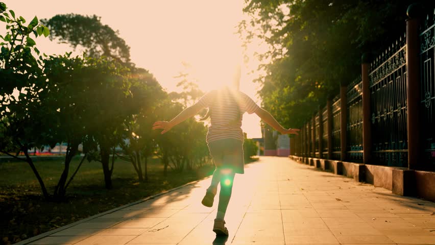 Superhero girl plays dreams of flying. Child runs along sidewalk on street in sun. Children dream, happiness concept. Joyful little girl runs at sunset in city park in spring. Happy Child play, dreams