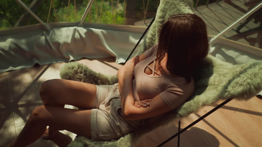 Lonely woman relaxes in armchair enjoying view from panoramic balcony window in country house surrounded by forest. Sun rays break through glass walls of terrace Royalty-Free Stock Footage #3472751303
