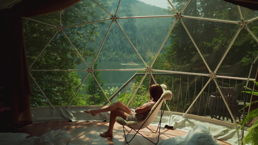 Woman sits alone at contemporary room with stunning mountain view. Brunette lady enjoys free time sitting in cozy armchair. Concept of escaping from everyday life