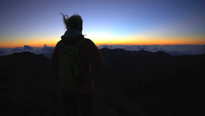 Silhouette of young female hiker watching the sunrise on the summit of Haleakala National Park on island of Maui