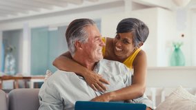 Mature couple at home with woman hugging and surprising man sitting on sofa using laptop - shot in slow motion - Powered by Shutterstock - Get 15% off with code: PIKWIZARD15