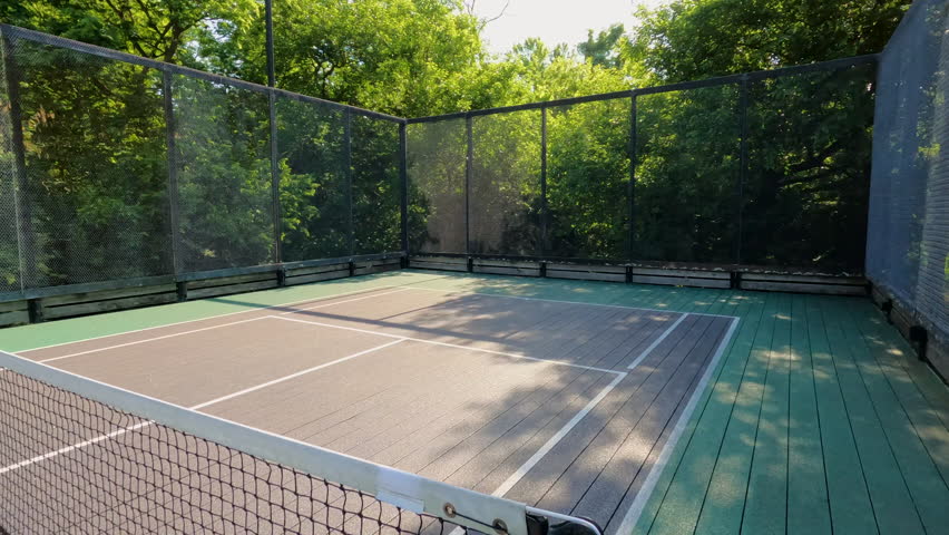 Pickleball or Paddle Tennis Courts. Elevated sport courts with nets in a public park setting. Courts are used for paddle tennis or pickleball play. Floor is green and blue with white boundary lines. Royalty-Free Stock Footage #3472788453