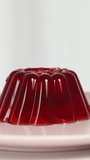 Vertical video. A cherry berry falls onto the red jelly, slowed down against a white background.
