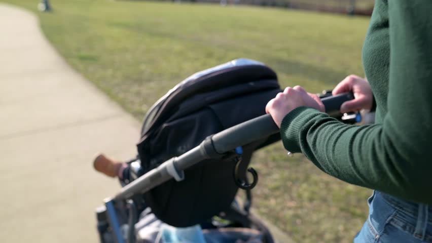 Mother pushing a stroller with a child, rear view with green sweater and jeans at the park Royalty-Free Stock Footage #3472930611